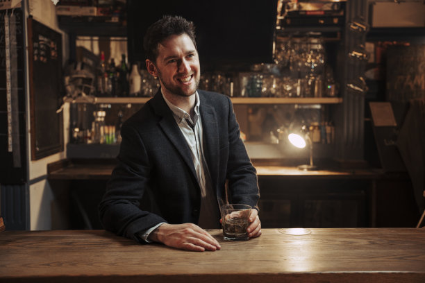 白人男性穿着西装，微笑着在酒吧喝威士忌图片下载