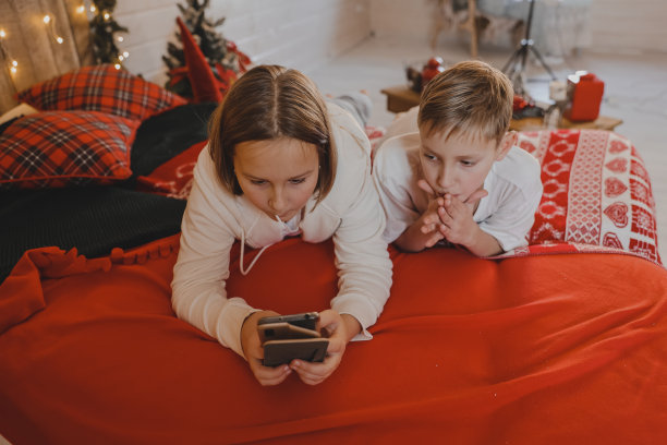 可爱的女孩和男孩在圣诞节的气氛中用智能手机聊天，新年装饰的房子，孩子和现代科技，沟通的概念。图片下载