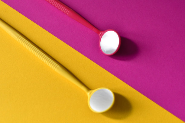 以黄色和粉红色为背景的两个牙科镜子的特写。本空间图片下载