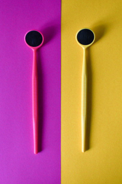 以黄色和粉红色为背景的两个牙科镜子的特写。本空间图片下载