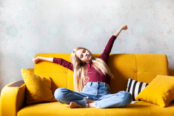 少女坐在舒适的黄色沙发上伸展身体。图片下载