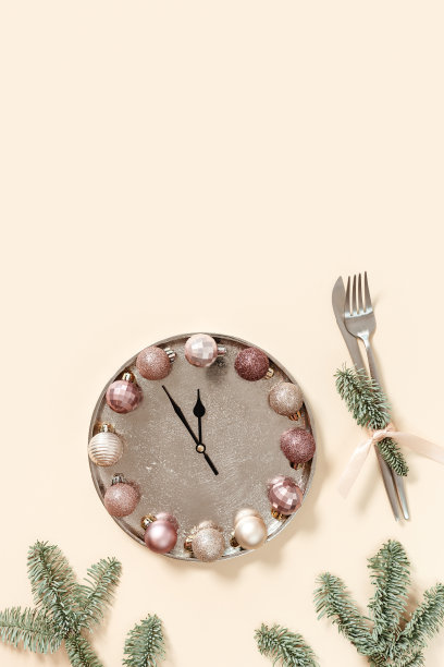 冬季节日餐桌布置概念，圣诞餐盘配时钟指针显示十二或午夜，米色粉色闪光球，刀、叉、冷杉树枝。新年节日食品概念图片下载