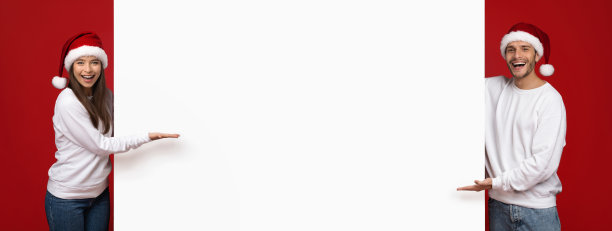 圣诞节的广告。一对戴着圣诞帽的快乐夫妇指着白色广告牌图片下载