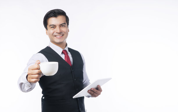 商务人士成功的技术沟通理念。自信正面英俊的商人拿着一杯咖啡或茶使用数码平板电脑，而站在孤立的白色背景。图片下载