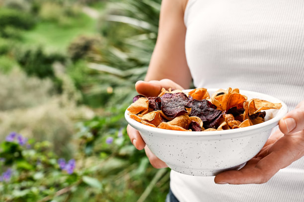 手拿着一个盘子，上面放着脆脆的蔬菜片，背景是大自然。素食点心。选择健康饮食。适当的营养。脱水蔬菜图片下载