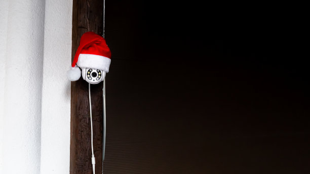 戴着红色圣诞老人帽子的白色闭路电视摄像机。户外视频监控。安全系统。副本的空间。网络摄像头街道控制。距离观看。智能技术，现代技术。新年假期概念图片下载