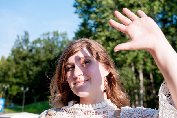 一个美丽的女孩，穿着白色的裙子，用她的手遮住她的脸，以自然为背景图片下载