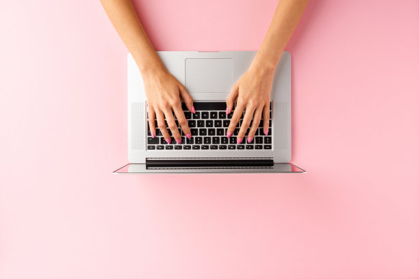 女性的手使用笔记本电脑在粉红色的背景和copyspace。办公桌面。俯视图图片下载