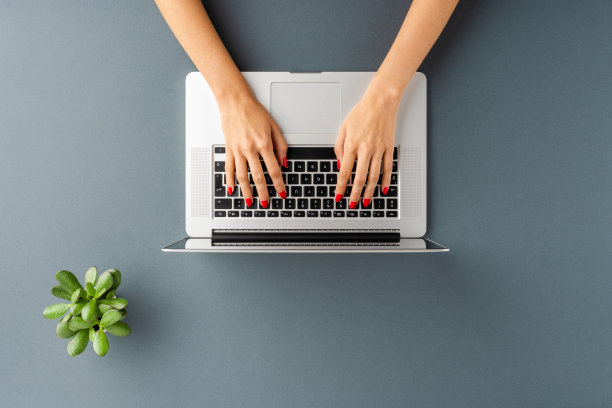 女性的手使用笔记本电脑在灰色的背景与绿色的花。办公桌面。俯视图图片下载