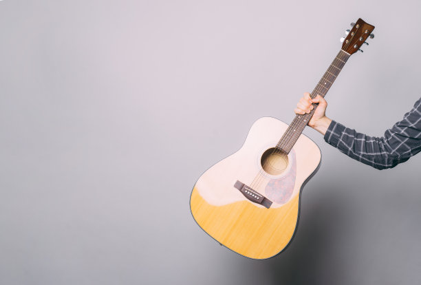 一张照片，一个男人的胳膊抱着一把吉他，靠近一堵灰色的墙图片下载