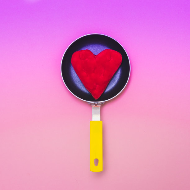 松软的红色枕头心形在黄色煎锅上梯度粉红色的背景。情人节快乐。图片下载