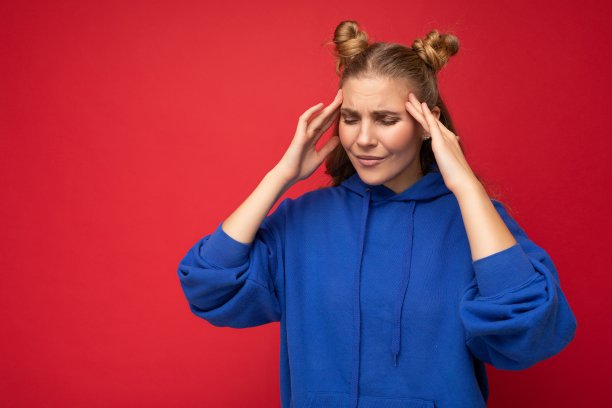 照片疲倦疲倦的年轻漂亮的金发女人与两个角真诚的情绪穿着休闲明亮的蓝色连帽衫隔离在红色的背景与复制空间和头痛。疼痛的概念图片下载
