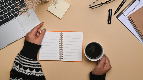俯视女性在毛衣拿着咖啡杯和阅读书的米色背景。图片下载