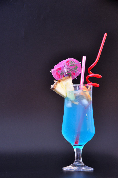 蓝色泻湖鸡尾酒，带饮料的高杯，菠萝片，吸管和黑色背景上的雨伞。图片下载