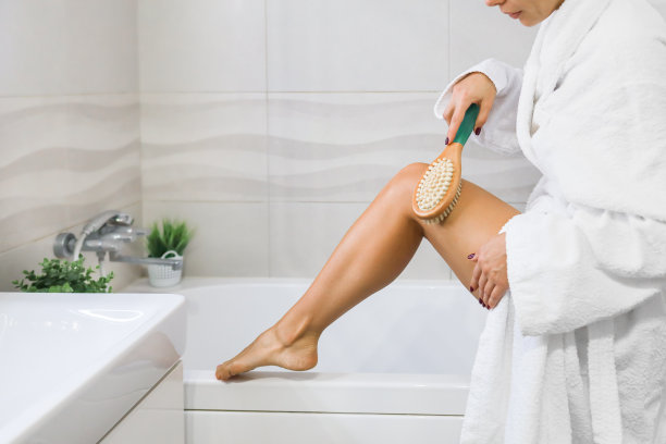 一名年轻女子在家中的浴室里用带有天然鬃毛的木刷进行按摩，这是身体护理的概念图片下载