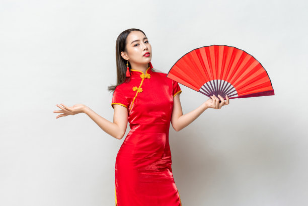 美丽的亚洲女人在红色东方风格旗袍穿着持扇在浅灰色孤立的背景图片下载