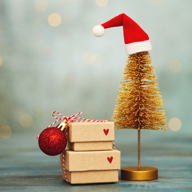 可爱的圣诞背景与堆叠的礼物和金色圣诞树戴圣诞帽。蓝色背景与串灯和复制空间图片下载