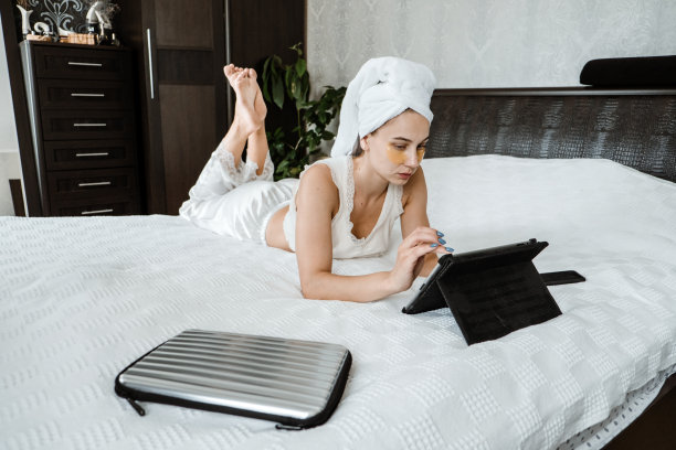 在家工作，在家自由职业，远程工作，电子学习，在线教育。快乐时尚的年轻女子穿着睡衣坐在白色的床上与平板电脑图片下载