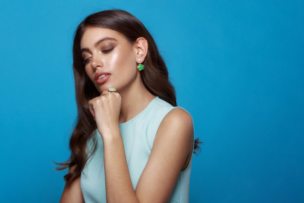 年轻女子穿着礼服，戴着饰品。珠宝耳环，珠宝戒指，在蓝色背景下看着相机。图片下载