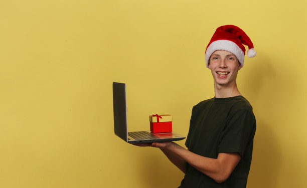 这个深思熟虑的男孩手里拿着一台笔记本电脑和一个礼品盒。图片下载