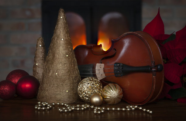 在燃烧的壁炉的模糊背景上，有小提琴、有机的树木雕像、小包和圣诞球的圣诞概念图片下载