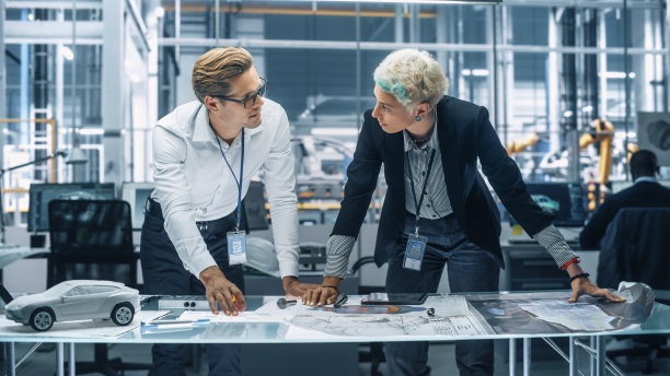 两个年轻的汽车工程师在汽车厂的办公室工作。工业设计师和同事讨论金属小齿轮在个人移动车辆的不同应用。图片下载
