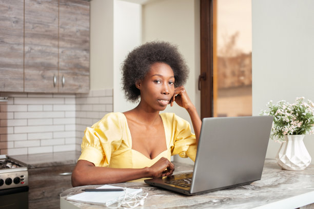 美丽的非裔美国自由职业者妇女肖像，餐桌在厨房。在室内用笔记本电脑工作。图片下载
