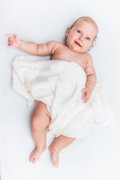 笑着的小女孩，躺在一张白色的床单上，盖着一块羊毛布图片下载