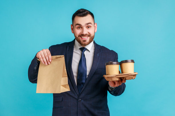 面带微笑的胡须男士身穿正装，手拿纸袋和外卖咖啡图片下载