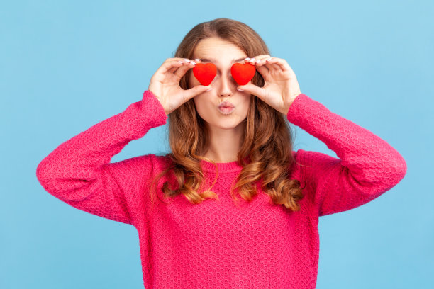 女人用小玩具心遮住眼睛，仿佛在看，情意绵绵，送出飞吻。图片下载