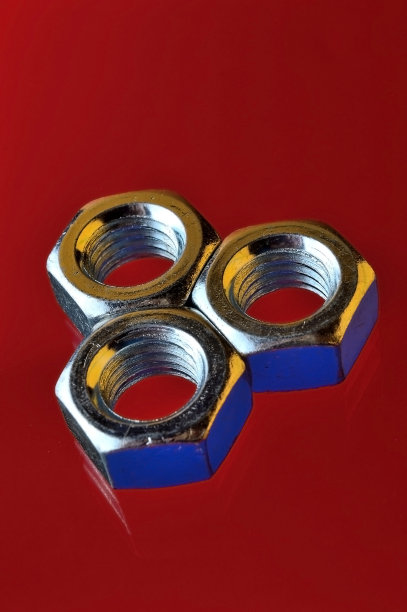 不同尺寸的镀铬金属螺母，用不同的颜色突出，摆放在红色的背景上。图片下载