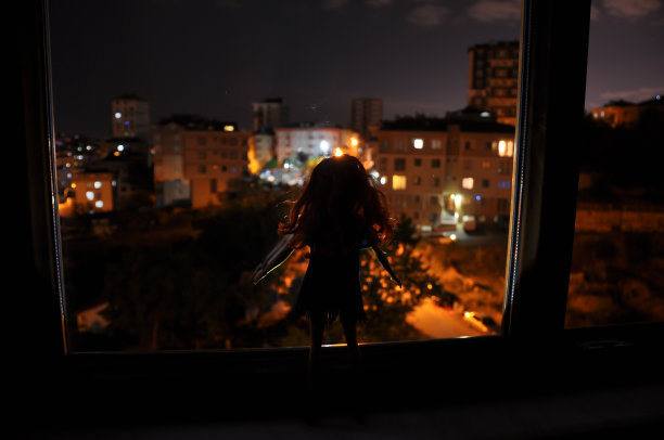 女性脸部在浅色背景下的剪影。一个孤独的长发娃娃的剪影，在夜晚的背光下，窗外的城市景色图片下载