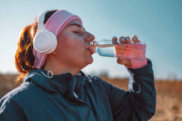 秋日阳光公园里，活跃的运动女性喝一瓶水，健康的生活理念图片下载