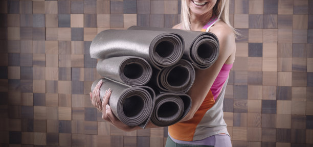 一位快乐的成年女性抱着一堆卷起来的瑜伽垫的图片。瑜伽和普拉提概念。训练、跳舞和造型。图片下载