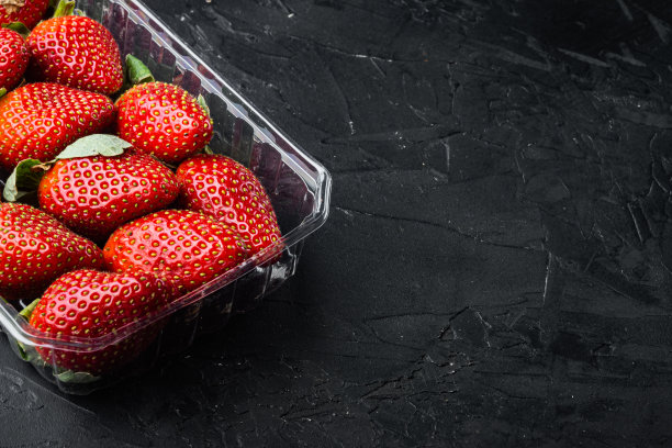 红色的成熟草莓在透明的塑料托盘上，在黑色的背景上有文字的复制空间图片下载