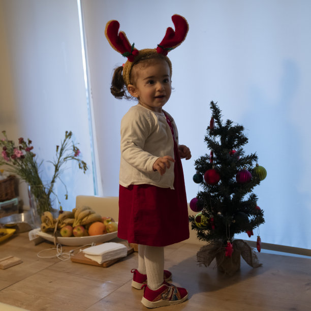 照片的蹒跚学步的女孩与服装驯鹿鹿角和圣诞树图片下载