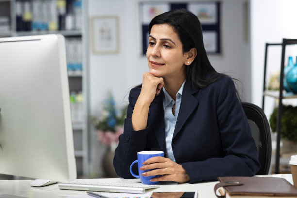 迷人的女商人坐在室内办公室的桌子上，工作。库存图片图片下载