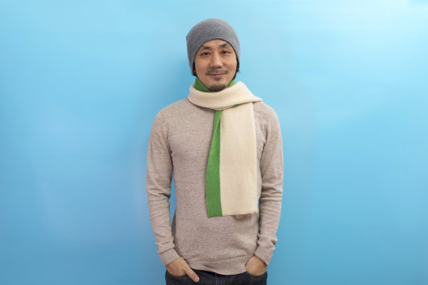 英俊的成年亚洲男子在冬季毛衣，围巾和帽子站在蓝色的背景。图片下载
