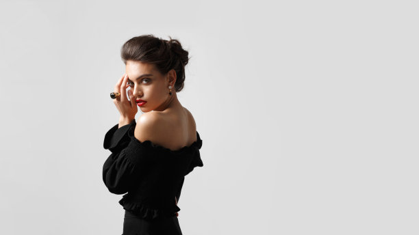 优雅的年轻女子化妆和发型，身穿黑色礼服，戴着豪华珠宝，在白色的背景。图片下载