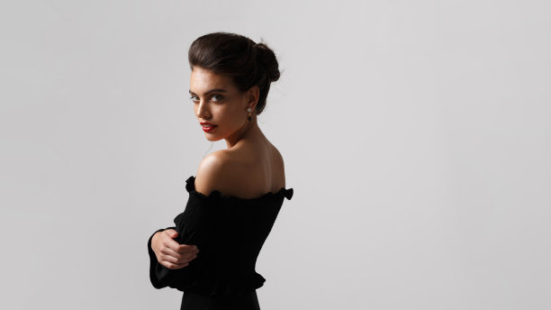 优雅的年轻女子化妆和发型，身穿黑色礼服，戴着豪华珠宝，在白色的背景。图片下载