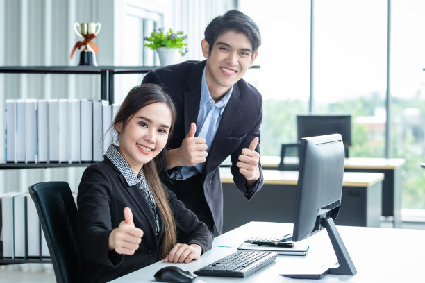 快乐的女商人和商人伙伴展示大拇指讨论积极的成人业务，在木制桌子上一起工作，在办公室背景下开会的想法。图片下载