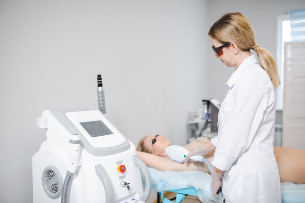照片的现代美容设备和女性皮肤科医生在保护眼镜执行一个程序的激光脱毛腋下的一个年轻女孩图片下载