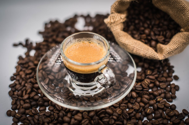一杯咖啡被放在从袋子里掉出来的咖啡豆中间。图片下载