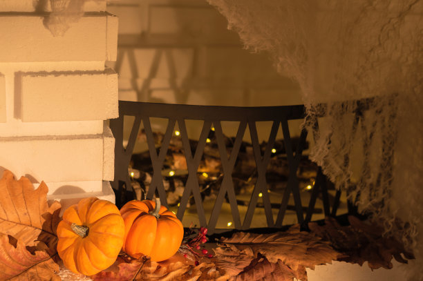 棕色叶子上的橙色南瓜，靠近模糊的壁炉，上面有蜘蛛网。有选择性的重点。秋天,万圣节的概念图片下载