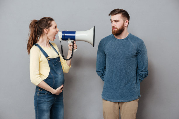 怀孕尖叫的女人拿着扬声器靠近严肃的男人图片下载