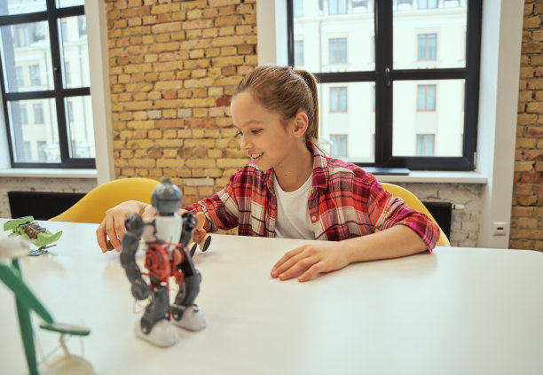 快乐的小女孩微笑着坐在桌旁，玩技术玩具，花时间在工程俱乐部图片下载