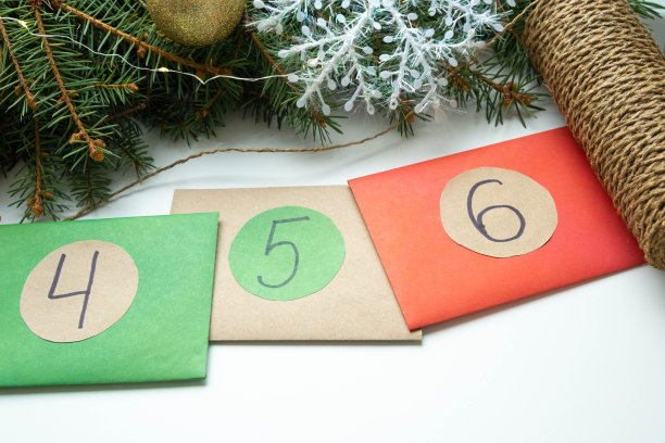 自制的圣诞节日历，彩色信封上的数字躺在白色的背景附近的绿色云杉树枝和球。关闭4,5,6号图片下载