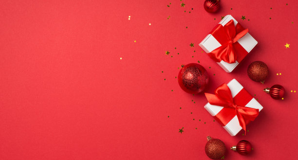 顶部全景照片白色礼品盒与红色缎子丝带蝴蝶结圣诞树球和金色的五彩纸屑在孤立的红色背景与copyspace图片下载