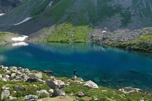 鸟瞰图的男子旅行者独自站在七彩湖附近的山区，夏季景观:高峰，雪，石头，五颜六色的山湖。Arkhyz高加索，卡拉恰-切尔克西亚图片下载
