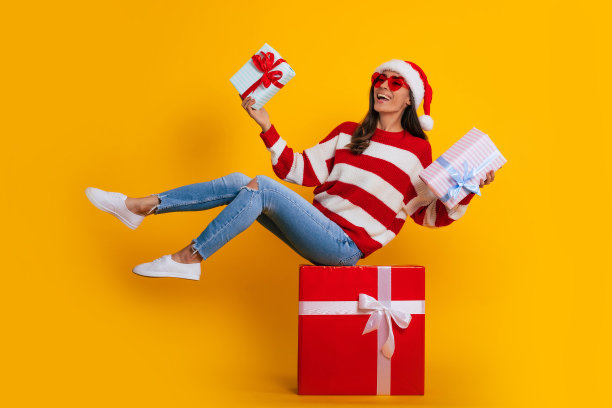 长照片兴奋的年轻微笑美丽和迷人的女人在圣诞帽和圣诞节心情，而她坐在大红色礼品盒和有乐趣图片下载